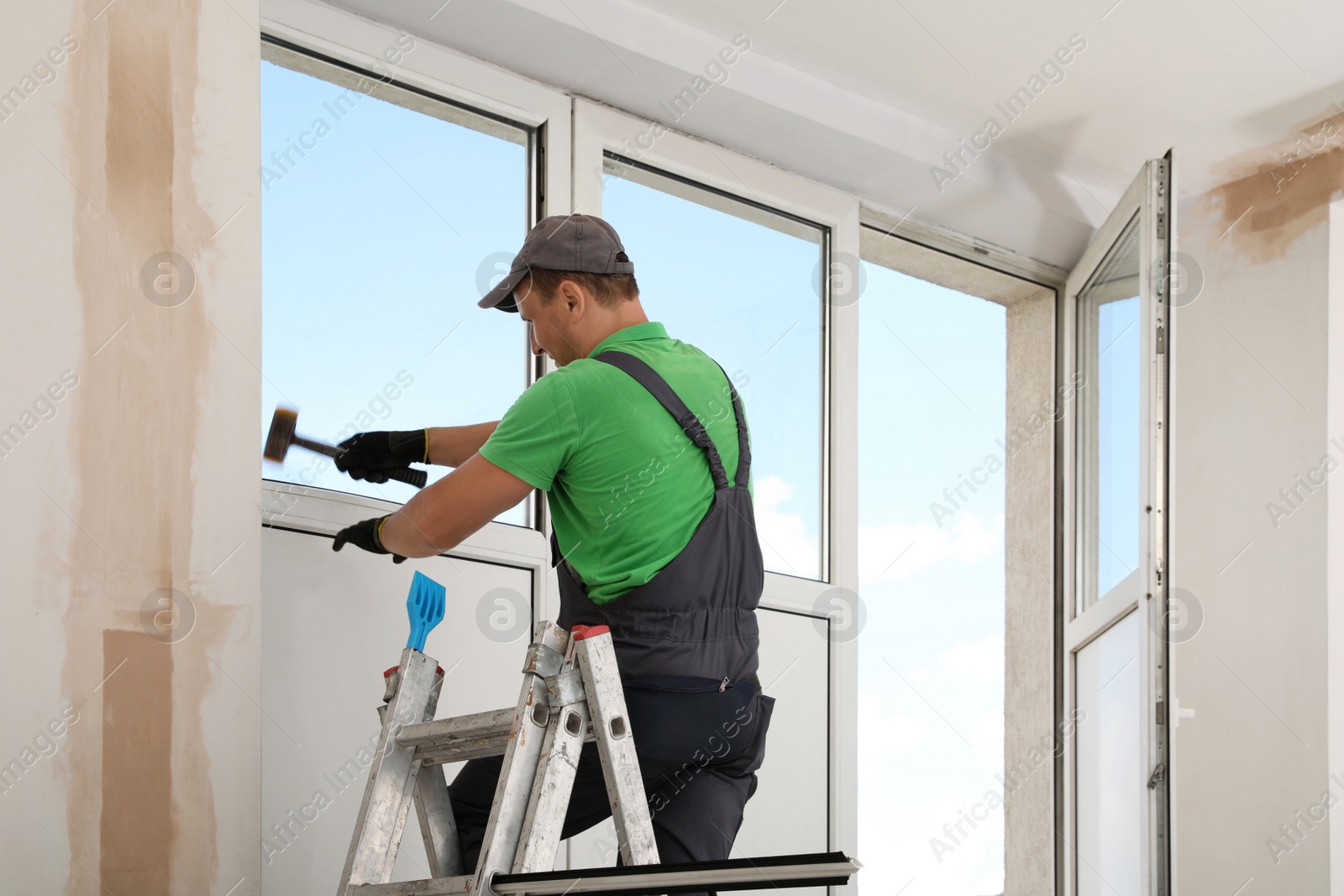 Photo of Worker on folding ladder installing window indoors