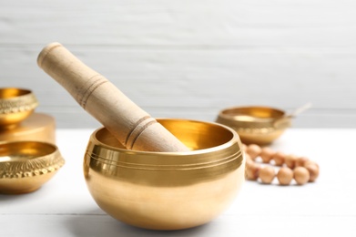 Photo of Golden singing bowl and mallet on white wooden table, closeup. Sound healing