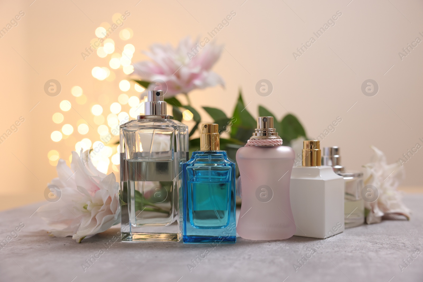 Photo of Perfume bottles and bouquet of beautiful lily flowers on table against beige background with blurred lights, closeup