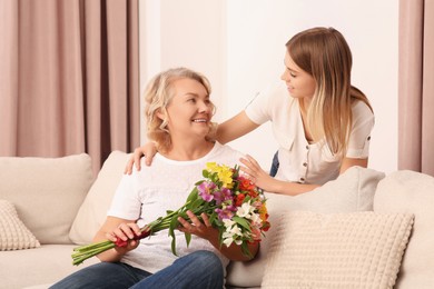 Photo of Young daughter congratulating her mom with flowers at home. Happy Mother's Day