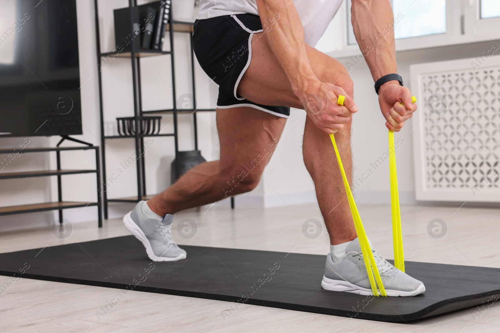 Photo of Athletic man doing exercise with elastic resistance band on mat at home, closeup