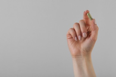 Photo of Woman holding vitamin capsule on grey background, closeup with space for text. Health supplement