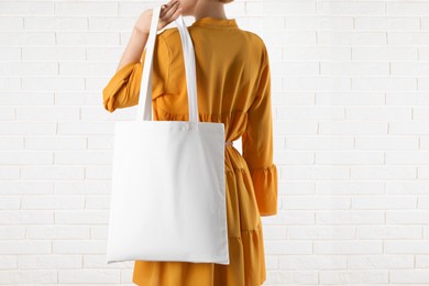 Photo of Woman with white textile bag near brick wall, closeup. Space for design