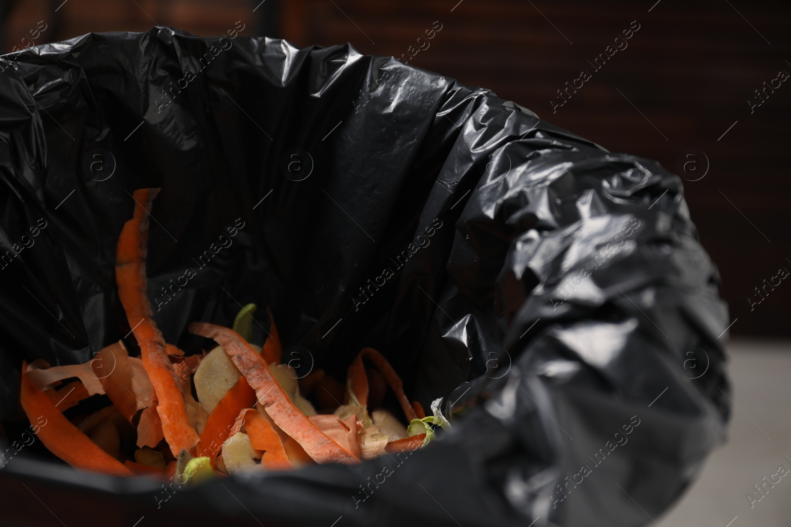 Photo of Garbage bin with peels of fresh vegetables indoors, closeup