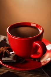 Cup of delicious hot chocolate, spices and coffee beans on wooden table