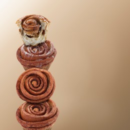 Cinnamon rolls balancing on light brown background, space for text