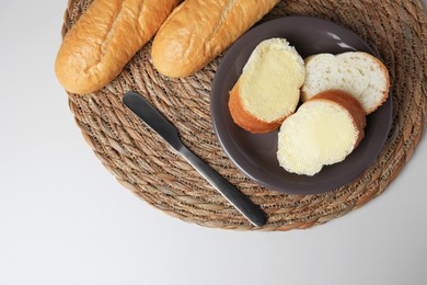 Photo of Whole and cut baguettes with fresh butter on white table, top view