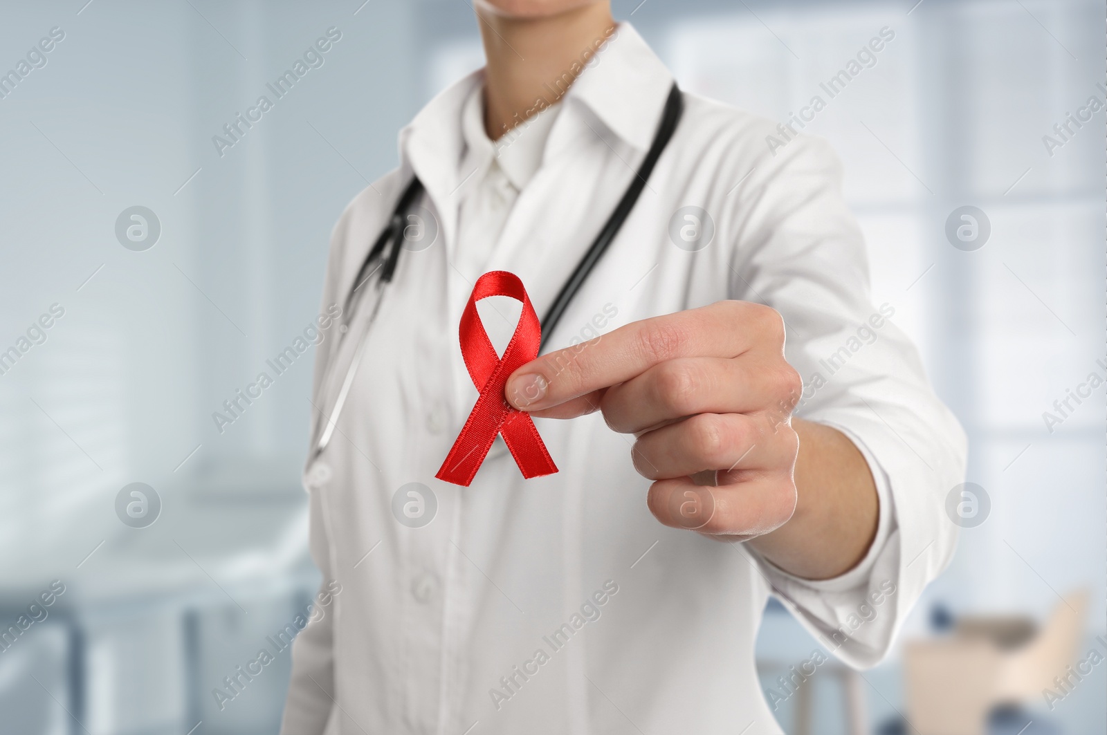 Image of Cancer awareness. Doctor holding red ribbon on blurred background, closeup