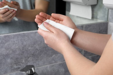 Woman wiping hands with paper towel in bathroom, closeup