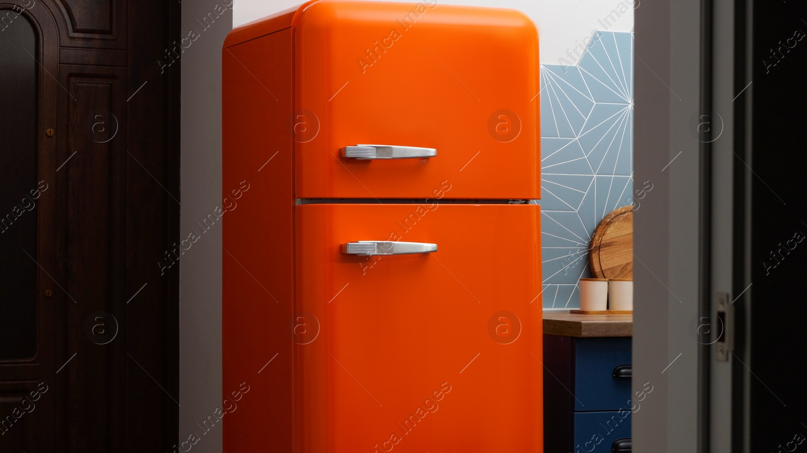 Photo of Modern closed refrigerator near colorful wall in kitchen. Domestic appliance