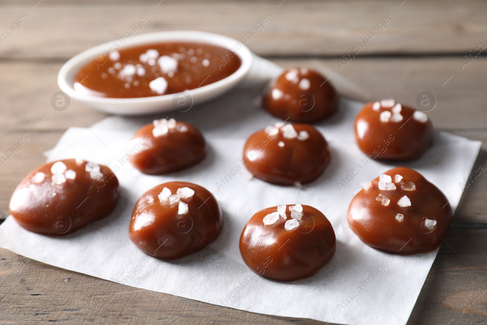 Photo of Tasty candies, caramel sauce and salt on wooden table
