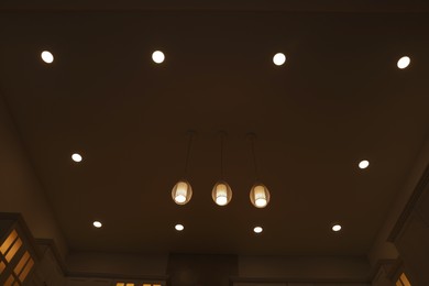 Photo of Ceiling with modern lamps and furniture in stylish kitchen at night, low angle view
