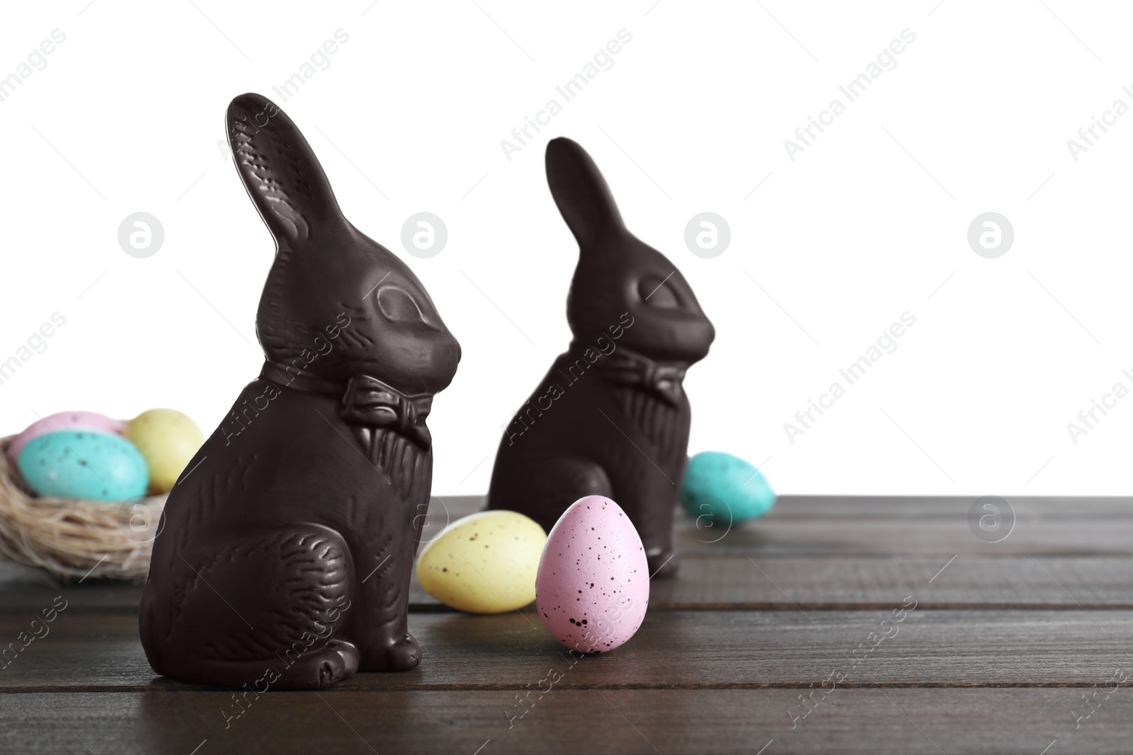 Photo of Dark chocolate Easter bunnies and eggs on wooden table against white background. Space for text