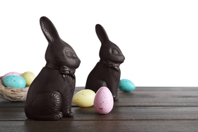 Photo of Dark chocolate Easter bunnies and eggs on wooden table against white background. Space for text