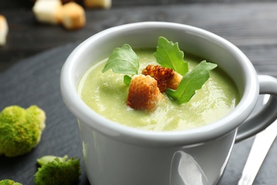 Photo of Cup of broccoli cream soup with croutons served on black table, closeup