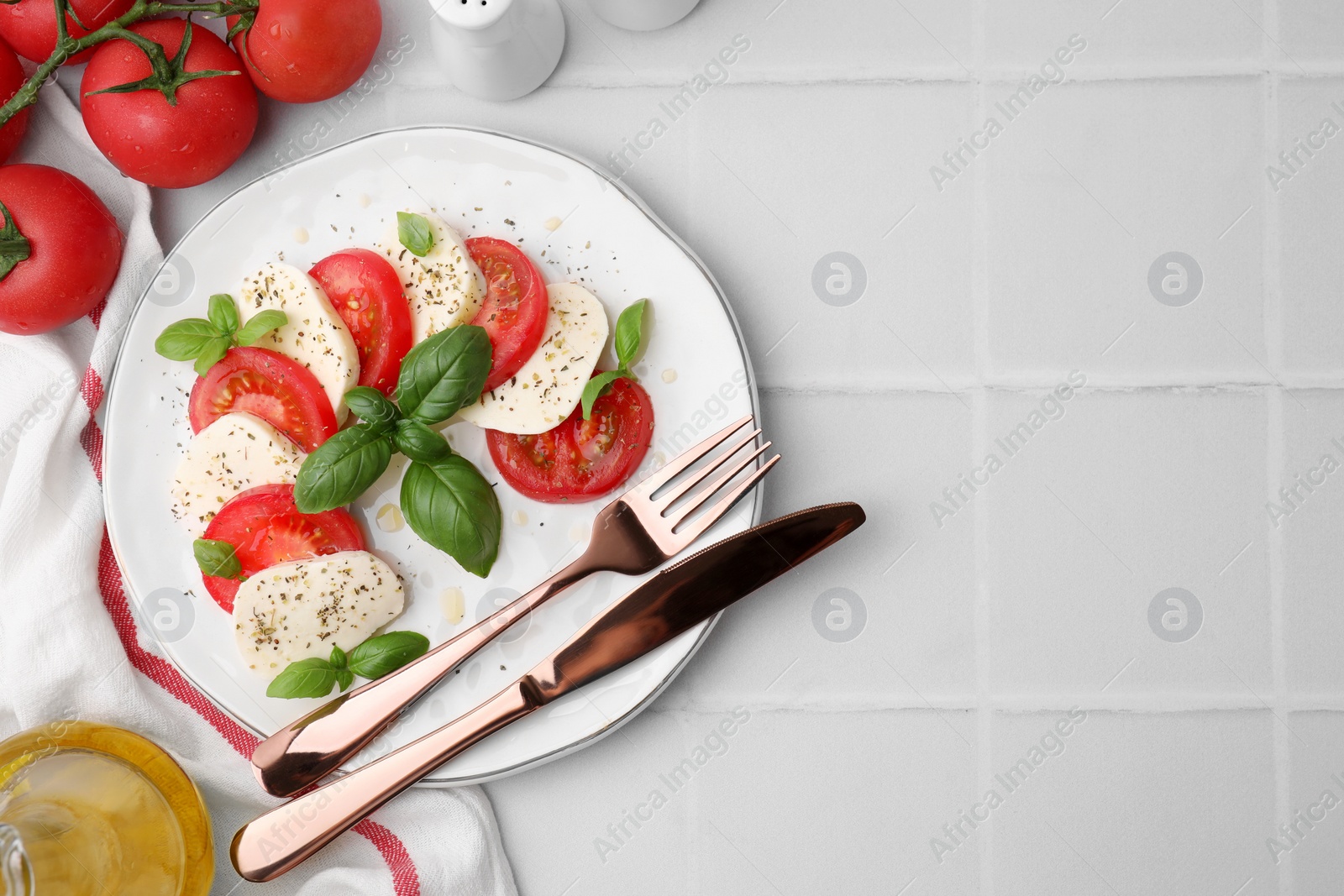 Photo of Caprese salad with tomatoes, mozzarella, basil and spices served on white tiled table, flat lay. Space for text