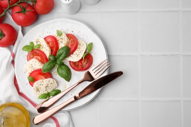 Photo of Caprese salad with tomatoes, mozzarella, basil and spices served on white tiled table, flat lay. Space for text