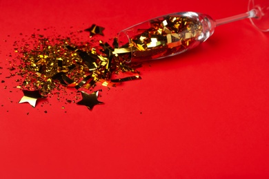 Photo of Champagne glass with golden confetti on red background, space for text