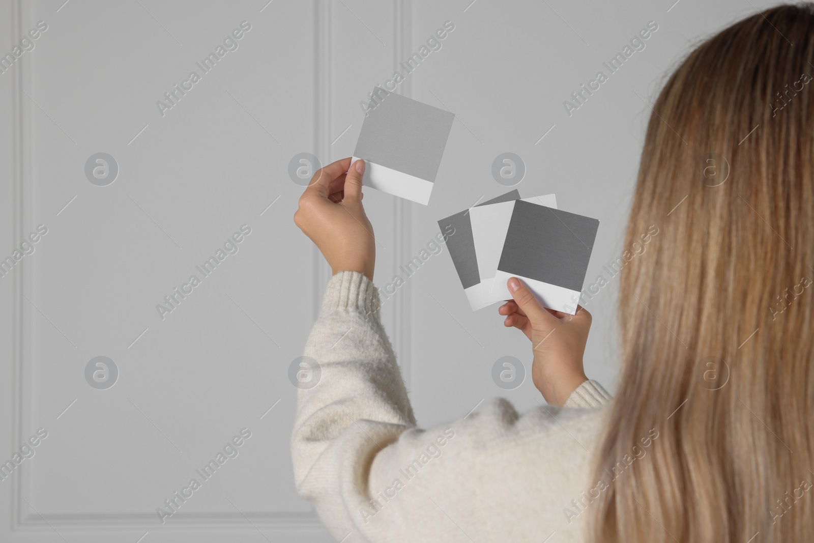 Photo of Woman choosing paint shade for wall indoors, focus on hands with color sample cards. Interior design