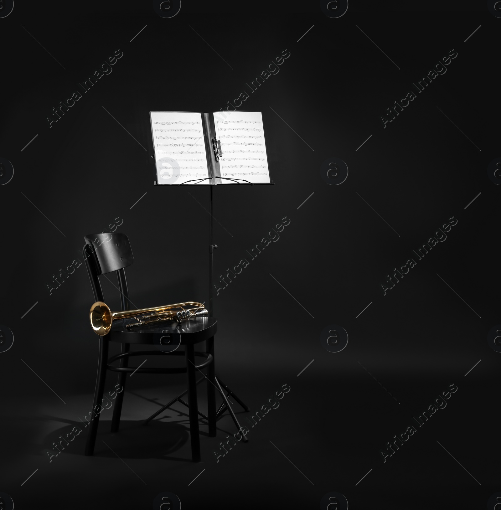 Photo of Trumpet, chair and note stand with music sheets on black background. Space for text