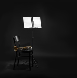 Photo of Trumpet, chair and note stand with music sheets on black background. Space for text