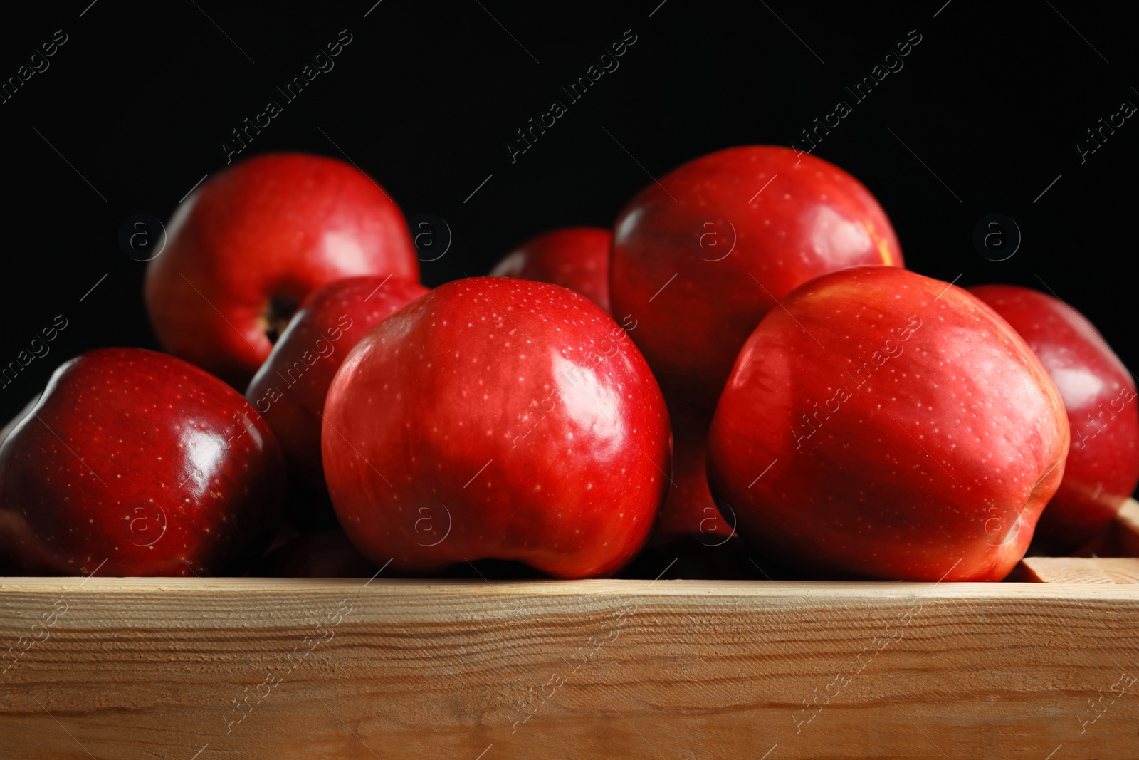 Photo of Wooden crate with fresh red apples on black background, closeup