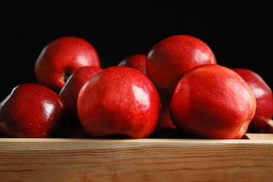 Wooden crate with fresh red apples on black background, closeup