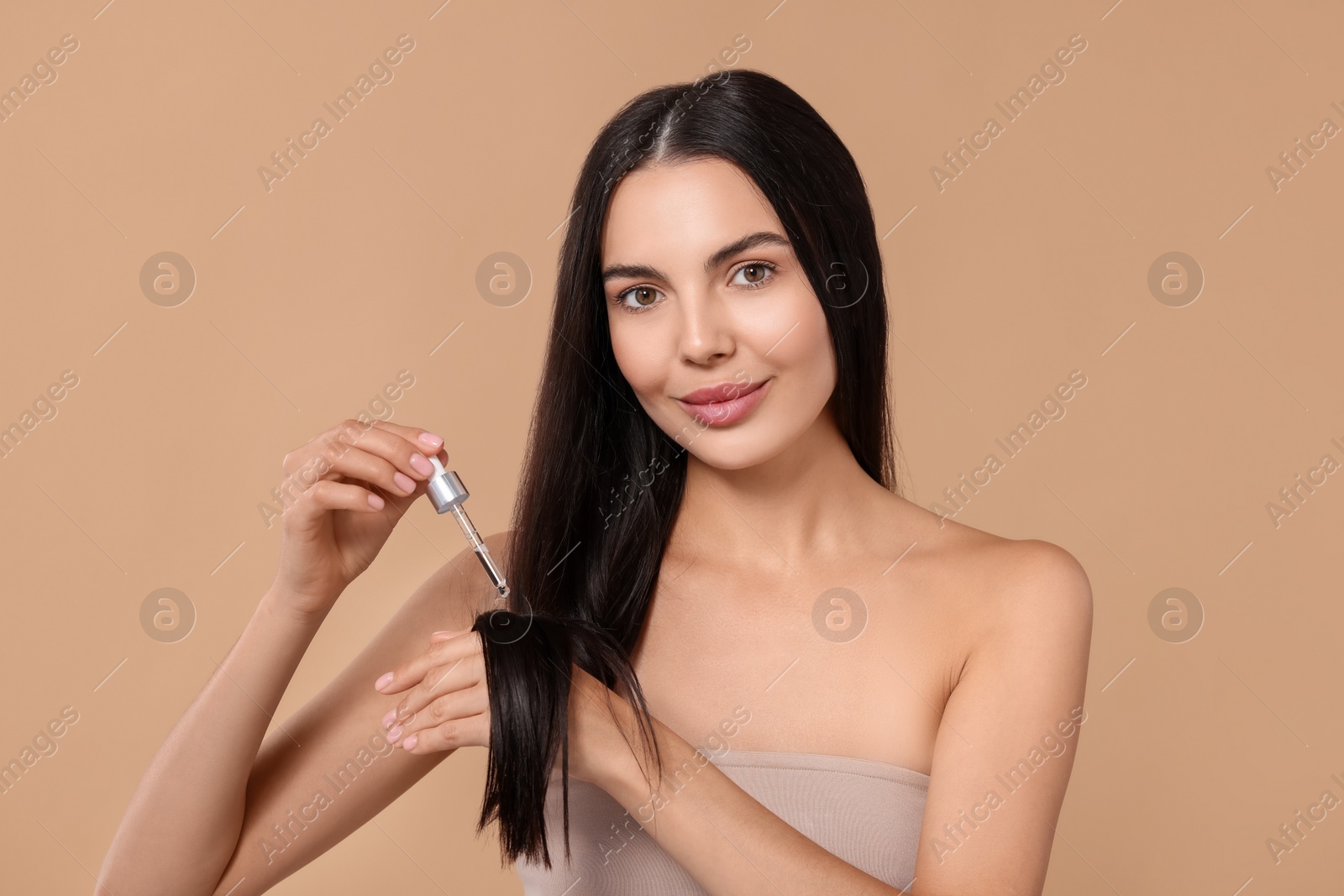 Photo of Beautiful woman applying hair serum on beige background. Cosmetic product