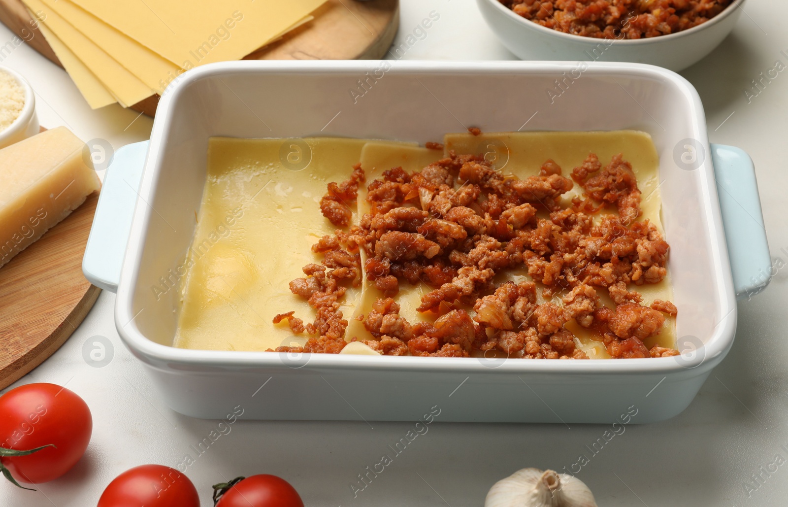 Photo of Cooking lasagna. Pasta sheets, minced meat in baking tray and products on white table, closeup