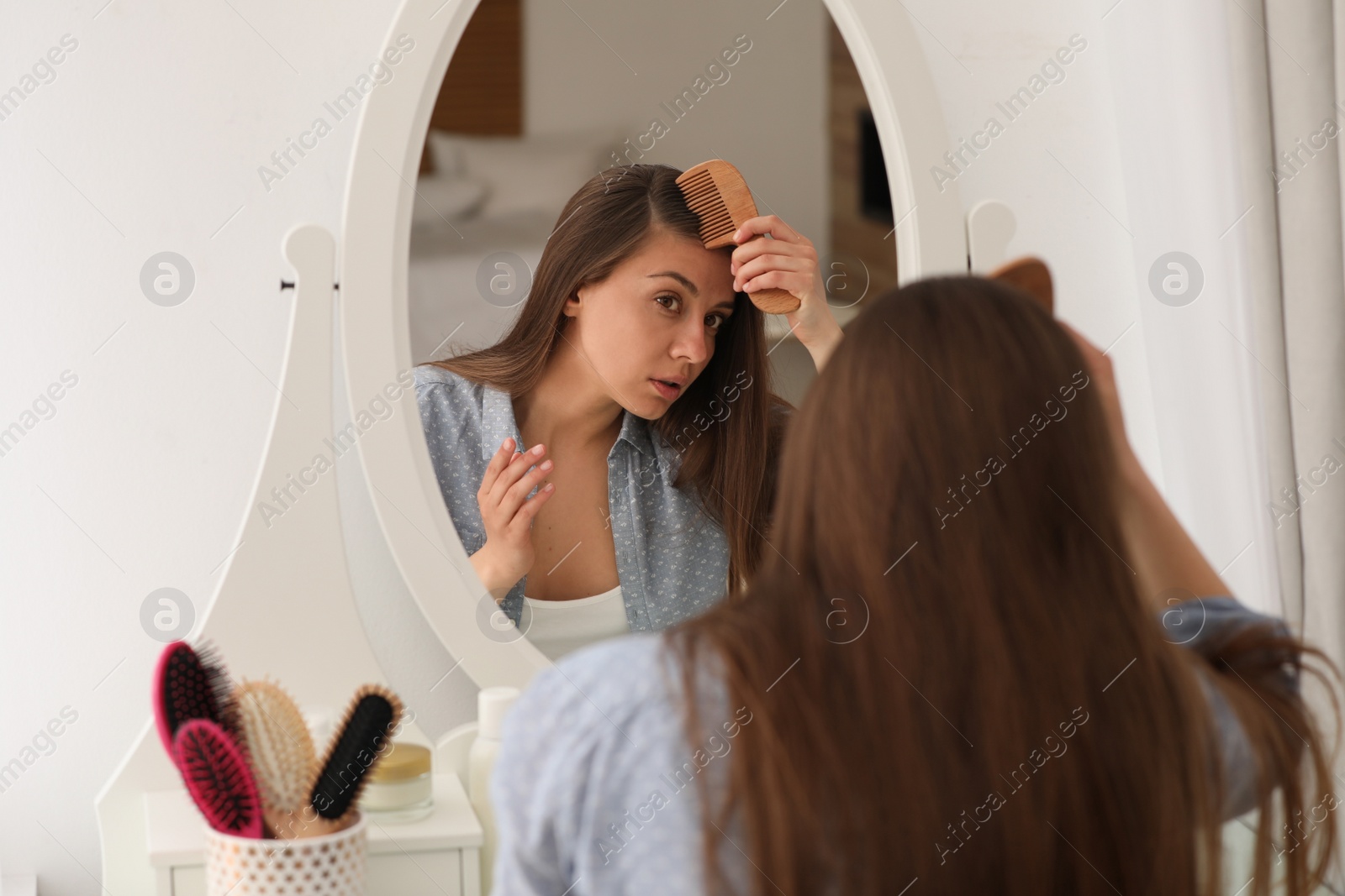 Photo of Young woman with hair loss problem near mirror indoors