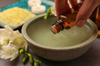 Photo of Woman dripping essential oil into bowl at grey table, closeup. Aromatherapy treatment