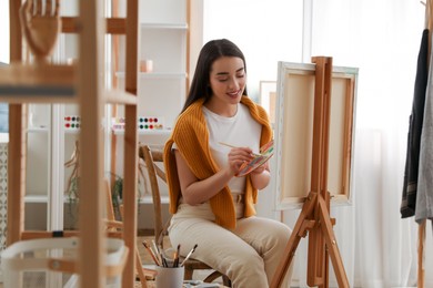 Beautiful young woman drawing on easel at home