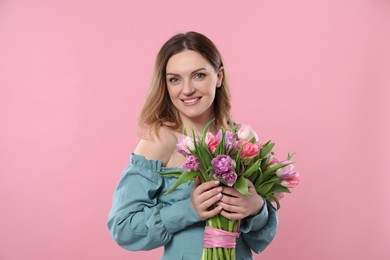 Happy young woman with bouquet of beautiful tulips on pink background