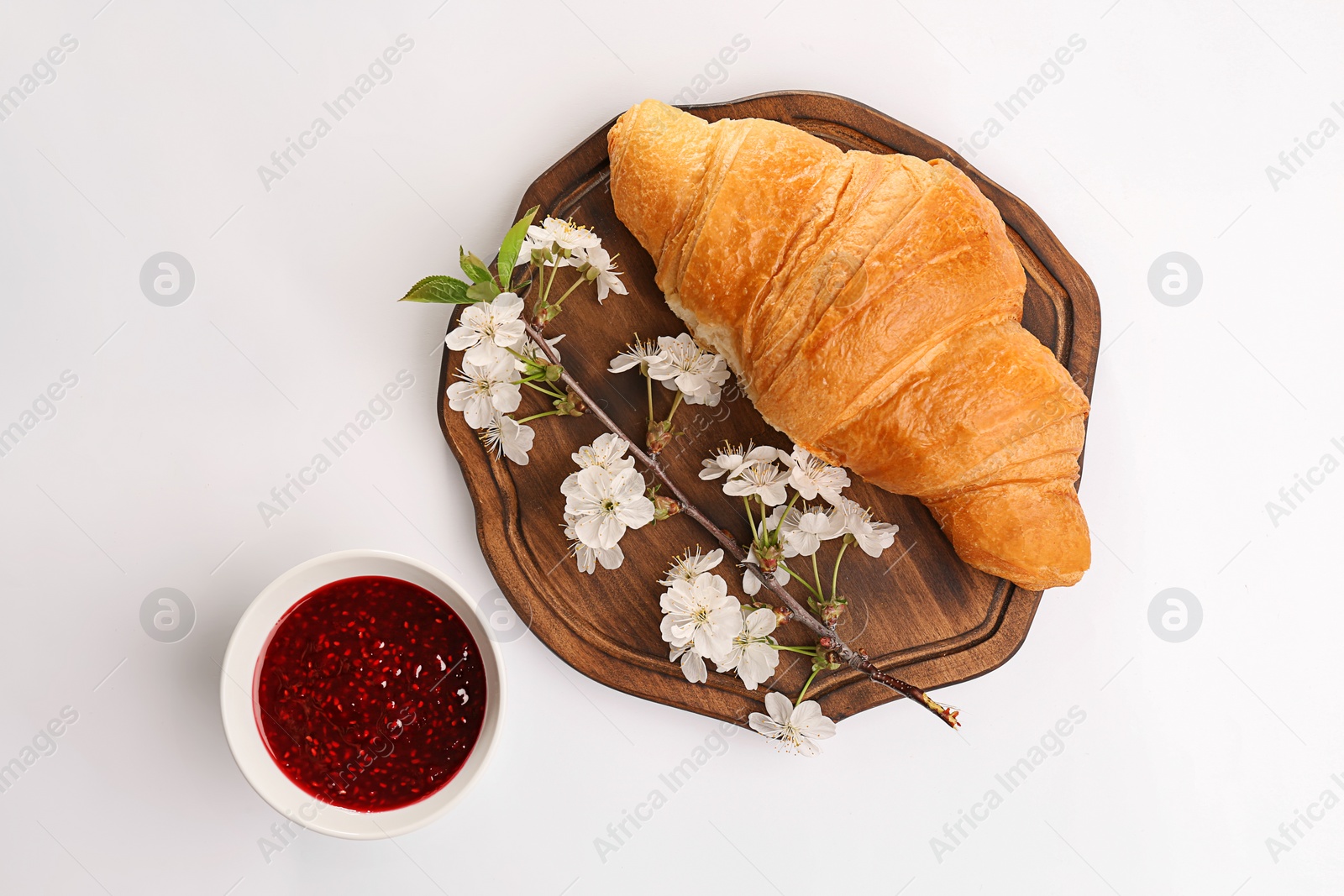 Photo of Wooden board with tasty croissant, branch and jam on white background, top view