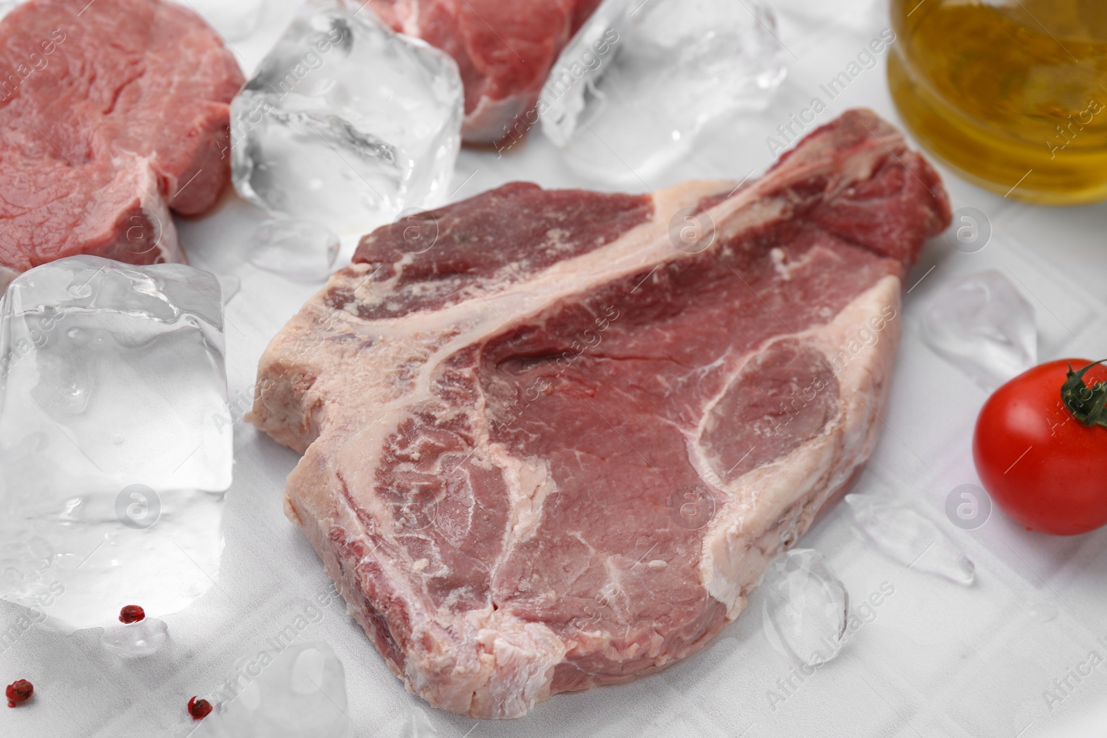 Photo of Fresh raw cut beef and ice cubes on white table, closeup