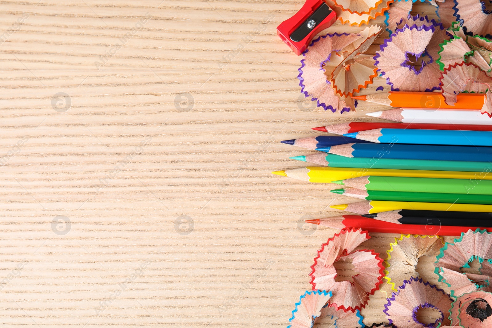 Photo of Color pencils, sharpener and shavings on wooden table, flat lay. Space for text