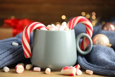 Photo of Cup of tasty cocoa with marshmallows and Christmas candy canes on wooden table against blurred festive lights