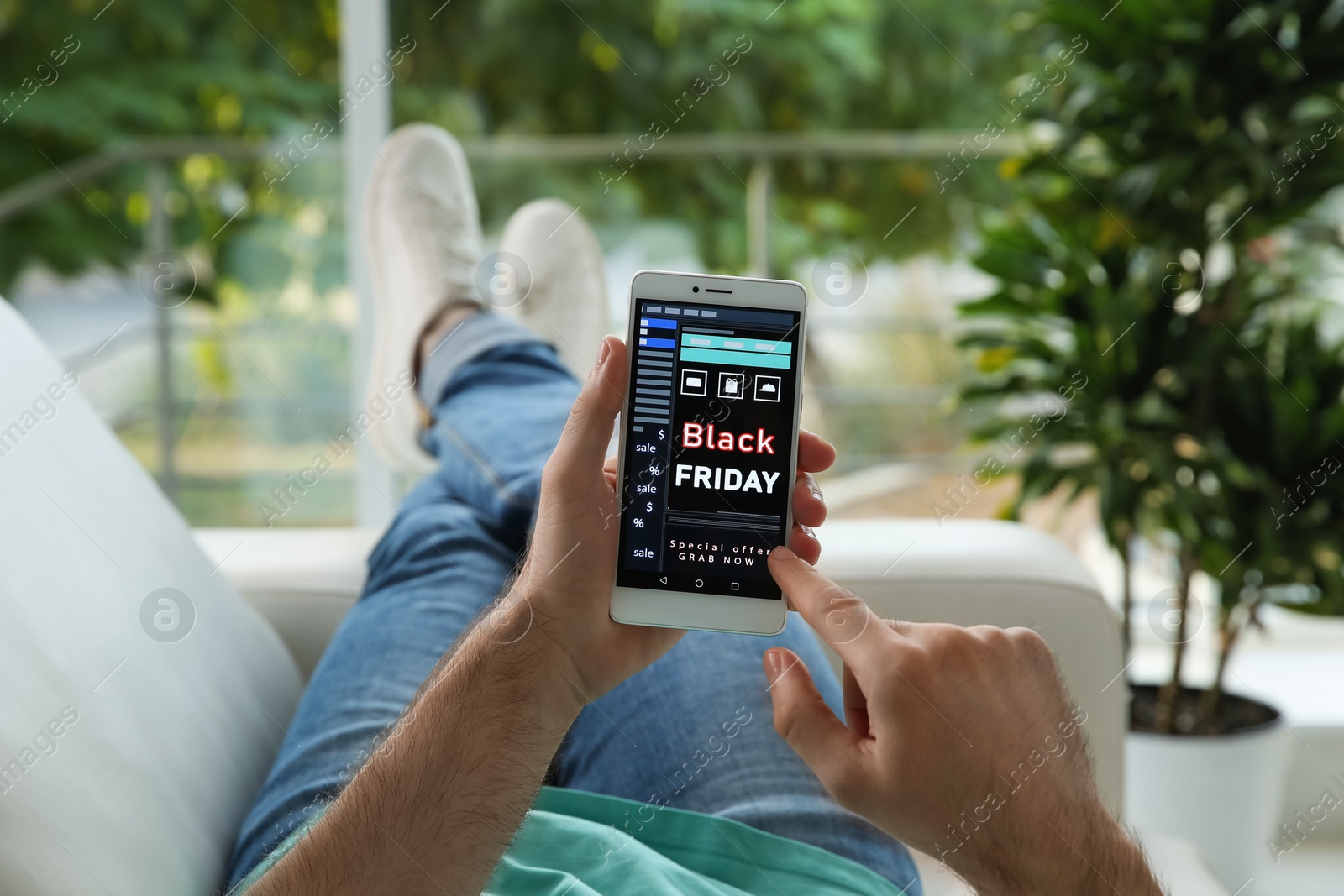 Photo of Man shopping online using smartphone on couch at home, closeup. Black Friday Sale