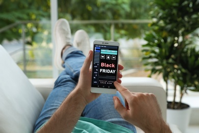 Photo of Man shopping online using smartphone on couch at home, closeup. Black Friday Sale