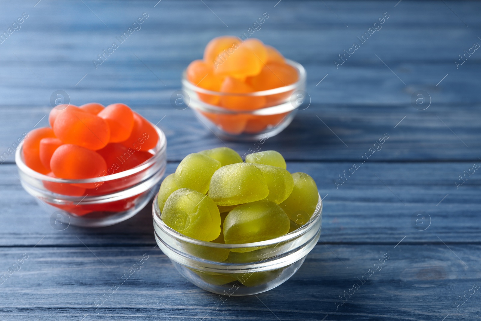 Photo of Glass bowls with tasty jelly candies on blue wooden table, space for text