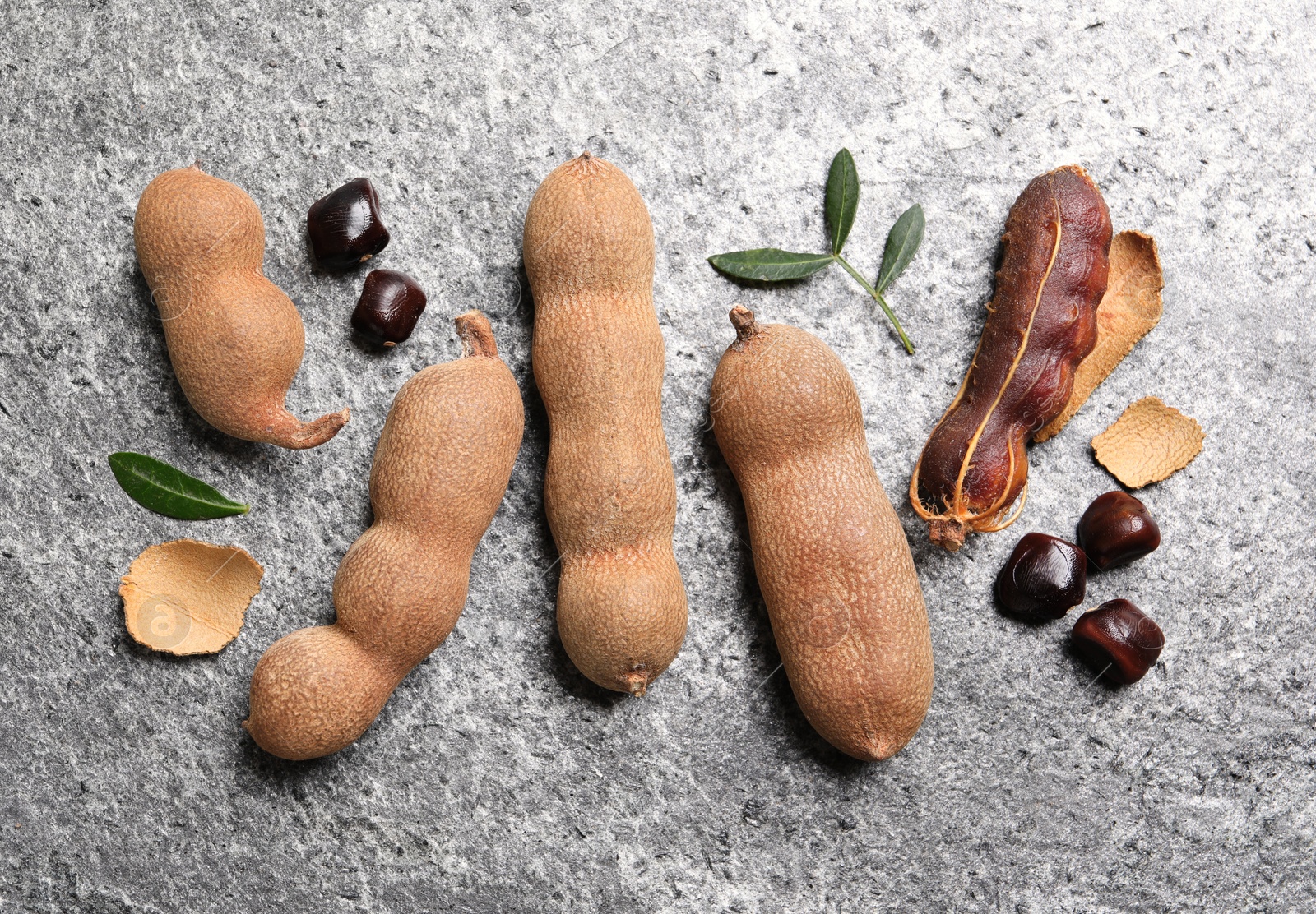 Photo of Delicious ripe tamarinds and leaves on grey table, flat lay