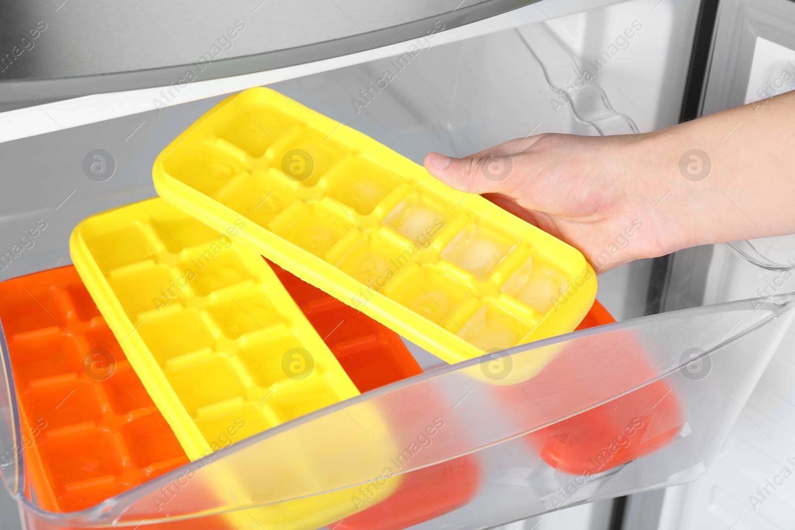 Photo of Woman taking tray with ice cubes from fridge, closeup