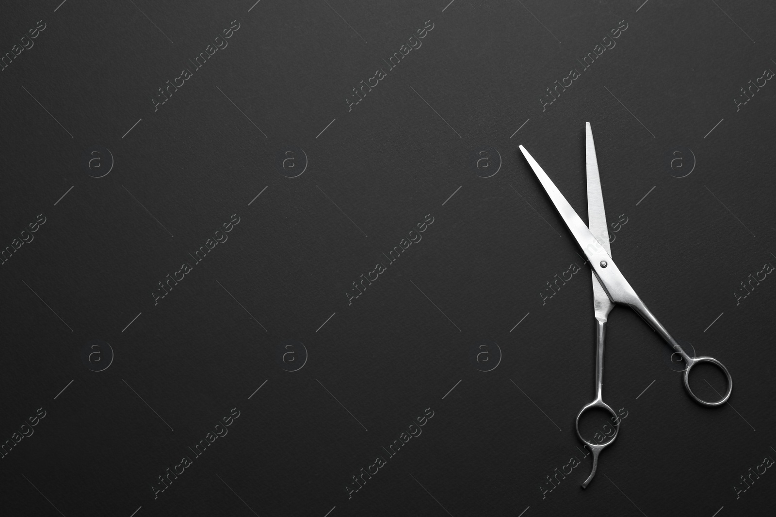 Photo of Hairdresser's scissors on dark background, top view. Space for text