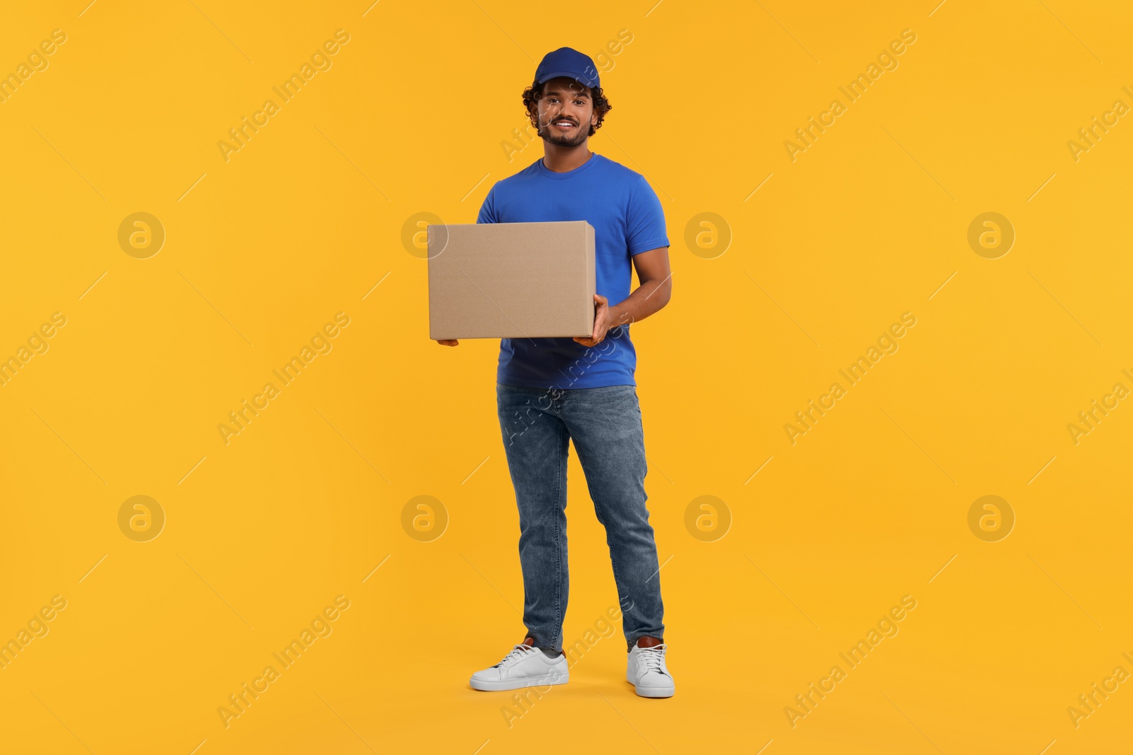 Photo of Happy young courier with parcel on orange background