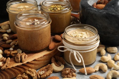 Tasty nut butters in jars and raw nuts on light grey table