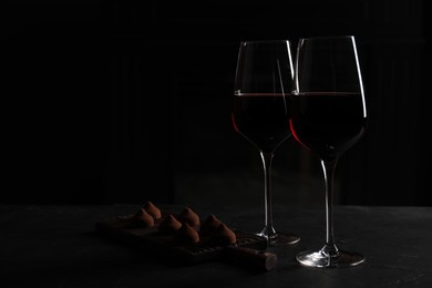Photo of Glassesred wine and chocolate truffles on black table in darkness, space for text