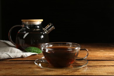 Cup of aromatic tea and teapot on wooden table