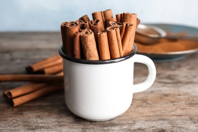 Photo of Mug with aromatic cinnamon sticks on wooden table