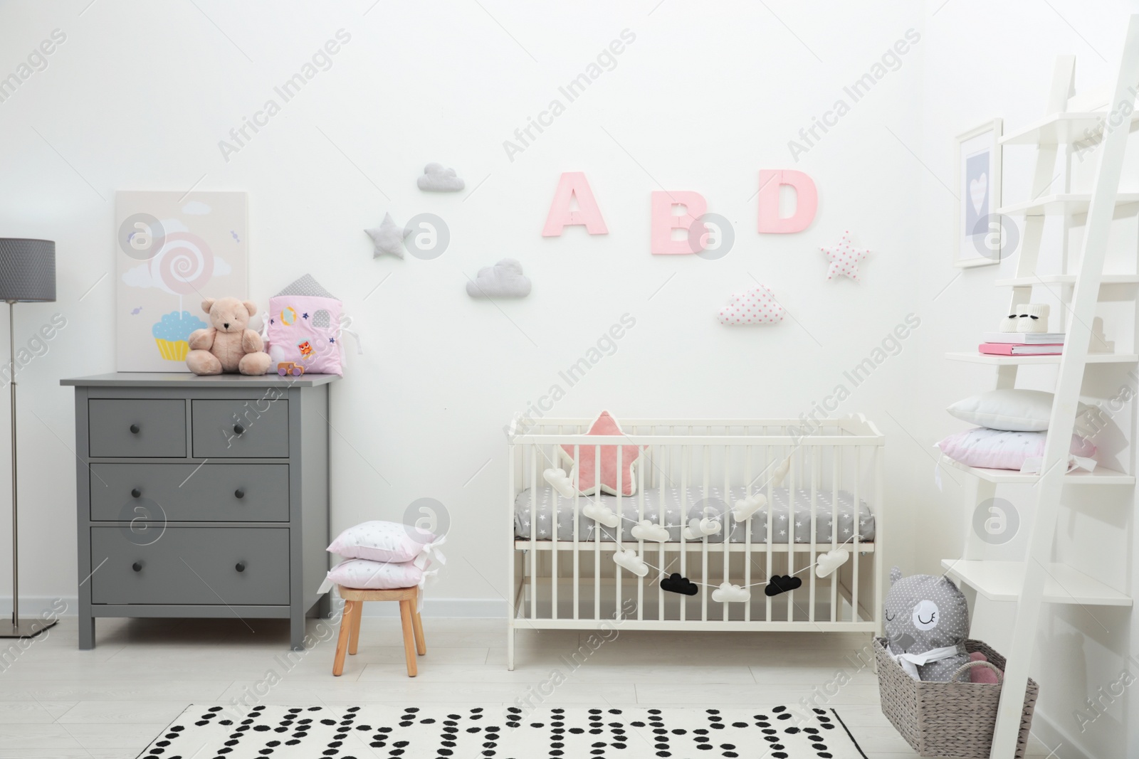 Photo of Cute baby room interior with crib and chest of drawers near white wall