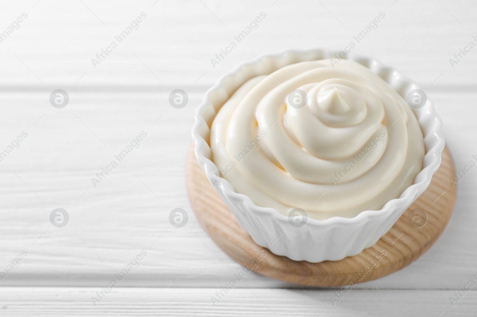 Photo of Fresh mayonnaise sauce in bowl on white wooden table, closeup. Space for text